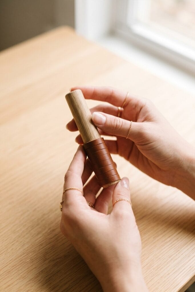 Female artisan hands holding a finished modern wall hook made of a wooden dowel tightly wrapped with a scrap leather strip.