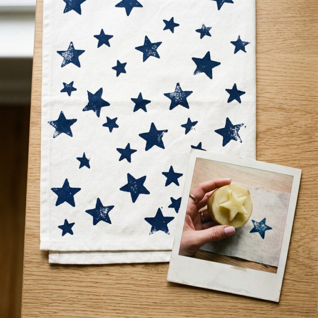 A playful natural cotton kitchen towel covered in a random night sky pattern of deep navy blue stars created using a rustic hand carved potato stamp technique