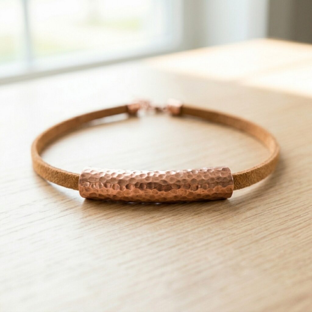 A perfectly square photo of a soft suede leather cord choker featuring a thick hammered copper tube (made from rolled copper sheet) in the center, resting elegantly on an oak table. Bohemian chic aesthetic.