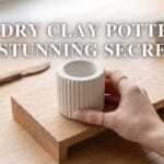 A blog cover photograph featuring a manicured hand placing a white fluted air dry clay pottery vessel onto an open studio display stand.