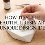 A manicured hand placing a finished clear botanical resin pendant onto a stand with blog title overlay.