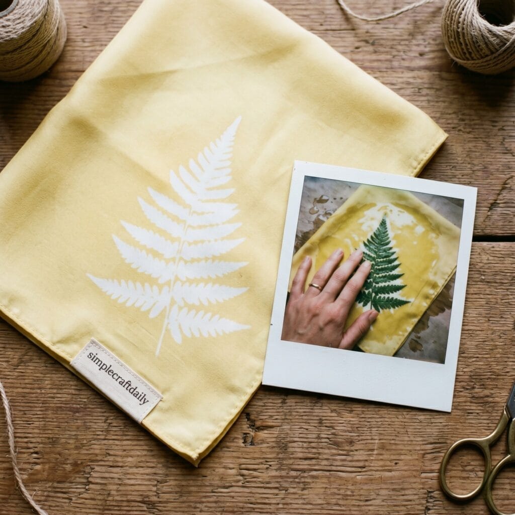 A pale yellow silk bandana with a white fern leaf silhouette next to a vintage polaroid photo capturing a single hand placing a real green fern leaf onto wet painted silk.