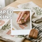 A wide blog featured banner with text reading 7 DIY STAMPED NAPKINS displaying a modern tablescape of terracotta arches olive branches and charcoal striped napkins on an oak table with a single polaroid snapshot
