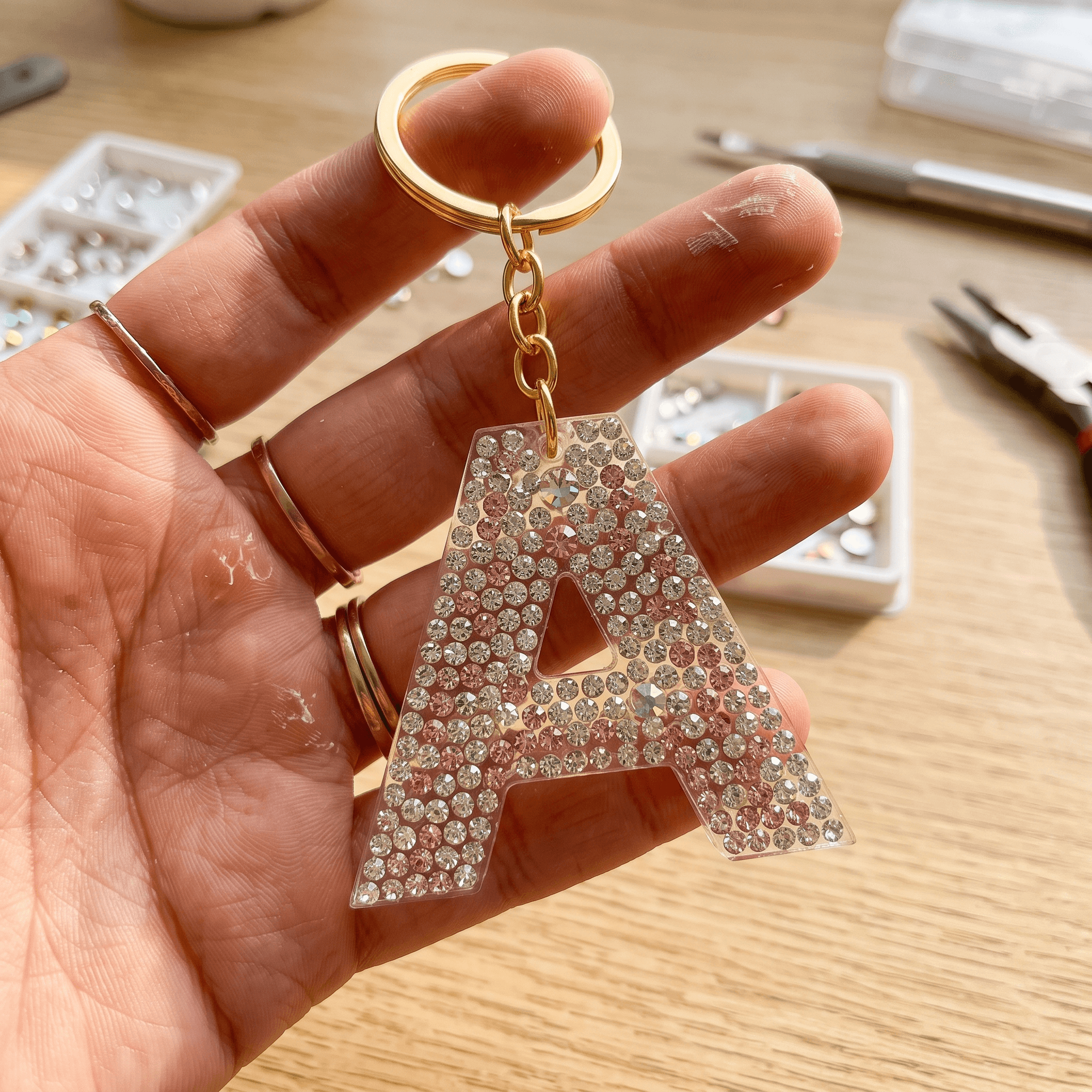 Hand holding a clear resin letter A keychain completely covered in pink and clear rhinestones.
