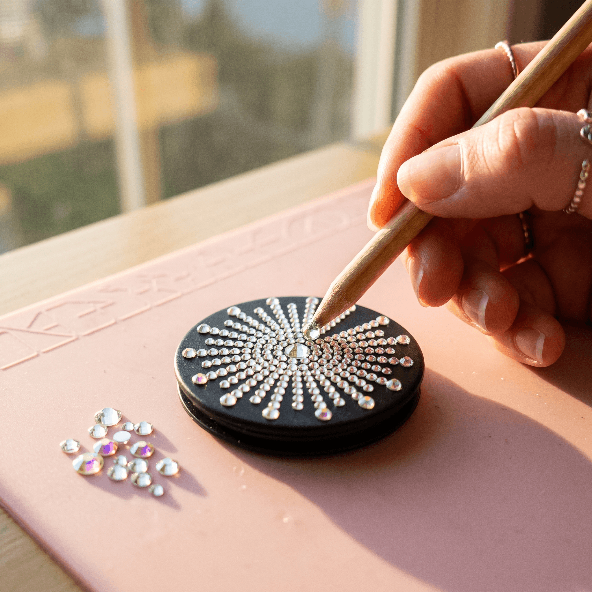 Decorating a black phone grip with a rhinestone sunburst pattern using a wax pencil.